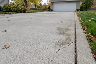 Localized crack and light surface wear along the edge of a concrete driveway.